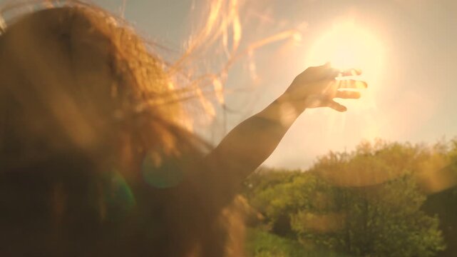 Girl with long hair sits in front seat of car, her hand out window and catching wind, glare of setting sun. Free woman driver rides car catches wind with her hand from car window. Woman travels by car