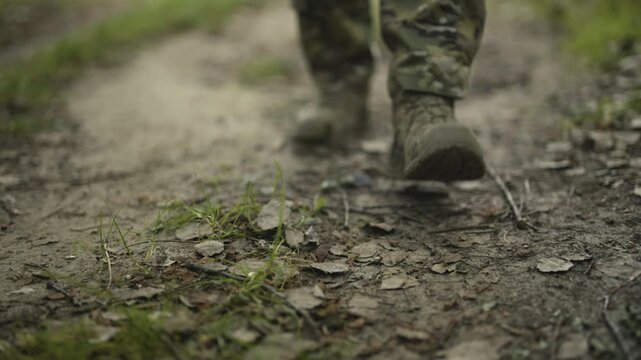 Camouflaged army soldier with AR15 carbine on a mission. Close-up legs walking down a dirt path