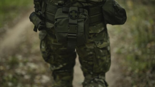 Camouflaged soldier with AR15 carbine on a mission. Close-up legs walking down a dirt path
