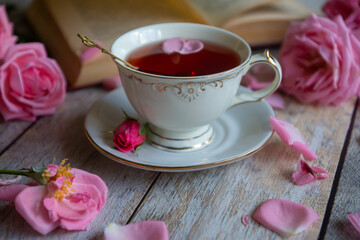 A cup of aromatic tea, a book and a rose on the table.