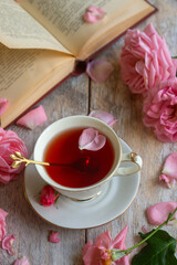 A cup of aromatic tea, a book and a rose on the table.