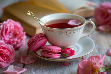 A cup of aromatic tea, a book and a rose on the table.