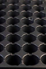 an empty plastic container with a large number of round holes for growing seedlings, a black plastic tray close up