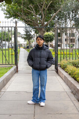 A teenager in a black jacket and blue jeans stands in front of a gate