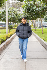 A teenager in a black jacket and blue jeans stands in front of a gate