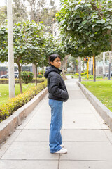 A teenager in a black jacket and blue jeans stands in front of a gate