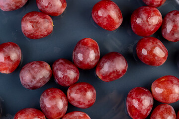 torn red ripe grapes in drops of water on a blue plate , wet ripe and delicious grapes on a plate on a black slate board