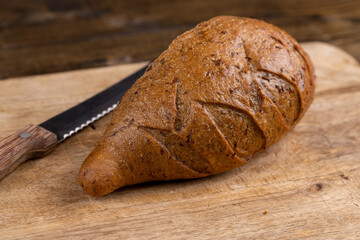 a whole small loaf of rye flour bread on the table on a cutting board, a small elongated loaf of freshly baked rye bread on an old cutting board for slicing bread