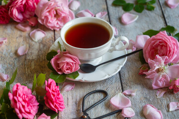 A cup of aromatic tea, a book and a rose on the table.