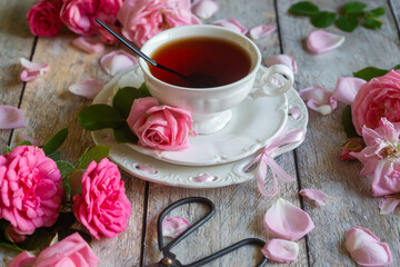 A cup of aromatic tea, a book and a rose on the table.