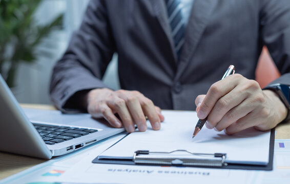 Businessman writing signature on contract at office desk, confirming agreement, approval, and compliance while managing legal paperwork and corporate administration.