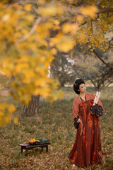 Woman in a beautiful autumn landscape wearing a traditional red dress, holding scrolls, standing gracefully.