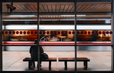 A solitary traveler at Prague's Vyšehrad station during early morning hours. Quiet atmosphere, minimalistic composition with emphasis on light and shadow.