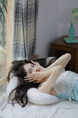 Woman in light blue top relaxing on a bed with soft pillows in a cozy room.