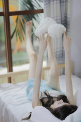 Young woman in blue dress playfully holding teddy bear while lying on bed.