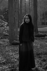 Woman in a long dark dress posing in a serene outdoor setting.