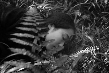 Woman lying in grass surrounded by ferns, conveying tranquility in a natural setting.