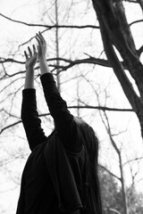 Woman stretching in nature with outstretched hands in a black jacket.