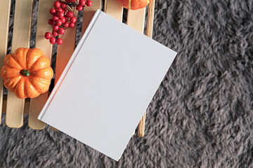 High angle view of white hard cover book on wooden decorative table with a pumpkin and red berries