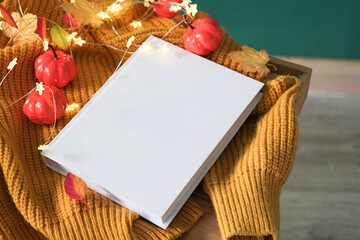 High angle view of white book on wooden decorative table with fairy lights , leaves and yellow sweater