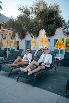 Summer Relaxation: A couple enjoys a day of leisure, basking in the sun on poolside lounge chairs, surrounded by the vibrant colors of summer.