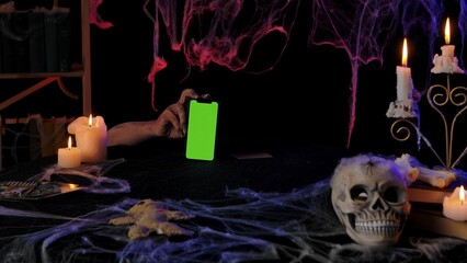 Scary zombie hands hold a smartphone with a green screen