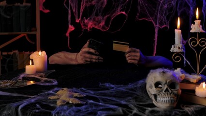 Scary zombie hands hold a smartphone and a bank card