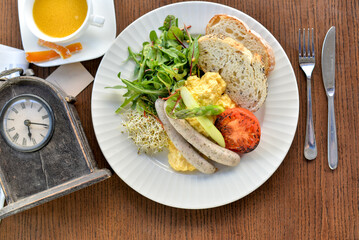 breakfast in a plate of sausages, omelette and tomatoes with herbs on the table