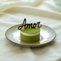 Round green tea cake with white cream layer and chocolate Amor inscription on a textured plate