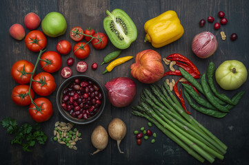 Fresh colorful assortment of fruits and vegetables including tomatoes, kiwi, bell peppers, berries, and greens on a dark wooden background, promoting healthy eating, organic living, and vibrant nutrit