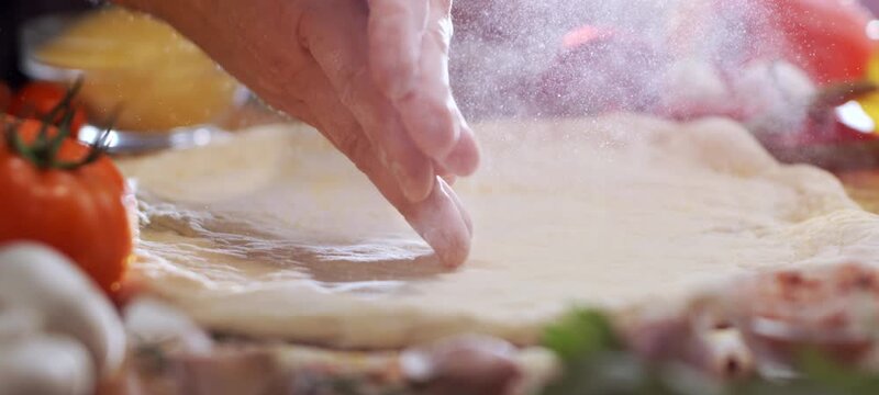 Vertical video of close-up of a professional pizzaiolo's hands sprinkling flour over fresh dough in a traditional pizzeria kitchen, preparing to make an authentic italian pizza with fresh ingredients