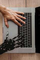 Human hand and robotic hand typing together on laptop, concept of AI collaboration, human-machine interaction, and future technology