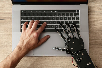 Human hand and robotic hand typing together on laptop, concept of AI collaboration, human-machine interaction, and future technology