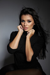 confident model showcases a striking look in a sleek black outfit. Her long hair flows softly as she poses gracefully, creating a captivating moment in a studio setting