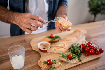 Man spreading pâté on baguette slices with fresh ingredients