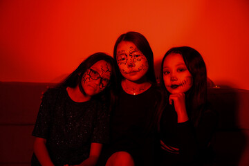 Three people in Halloween costumes are sitting with a glowing jack-o'-lantern