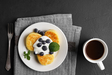 Cottage cheese pancakes served with curd and frozen blueberries, top view flat lay on black background