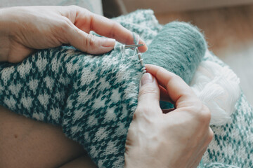 Norwegian knitted pattern in woman hands. Girl holding knitting needles and beautiful knitting pattern. Woman with white and azure knitted pattern. Knitting hobby. Knitwear concept. Spot sweater