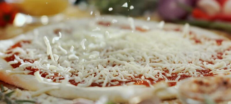 Close-up of a chef sprinkling delicious grated mozzarella cheese over a raw pizza base with fresh tomato sauce, preparing a traditional italian meal in a professional kitchen or pizzeria