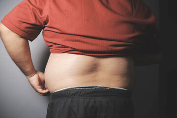 Naklejka premium Asian fat man in front of a mirror looks at his body. Excess belly fat, Unhealthy lifestyle, Diet concept.