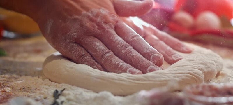 Close up view of a baker's hands kneading fresh raw pizza dough on a wooden board covered with flour, preparing a traditional italian dish in a pizzeria kitchen with warm lighting