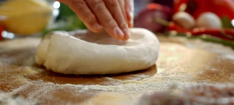 Male pizzaiolo's hands skillfully kneading and stretching fresh pizza dough on a wooden board dusted with flour, preparing an authentic italian meal in a traditional restaurant kitchen