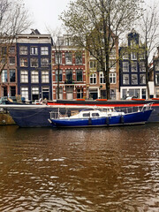 Panoramic view of Dutch facades, houseboats, and boats in the canals on a gray, overcast day. Urban planning and culture of the Netherlands.