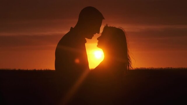 Silhouettes of a man and woman against the backdrop of sunset, lovers in an intimate moment. Concept love story. Super slow-motion shot.
