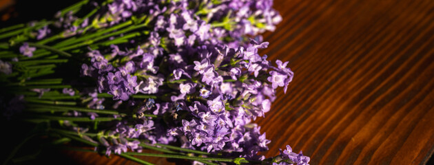 A fragrant bouquet of fresh purple lavender lies elegantly on a rustic wooden surface, illuminated...