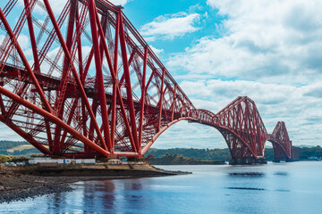 Red Forth Bridge in Edinburgh with view of the sea under clear blue sky, iconic Scottish landmark and coastal scenery