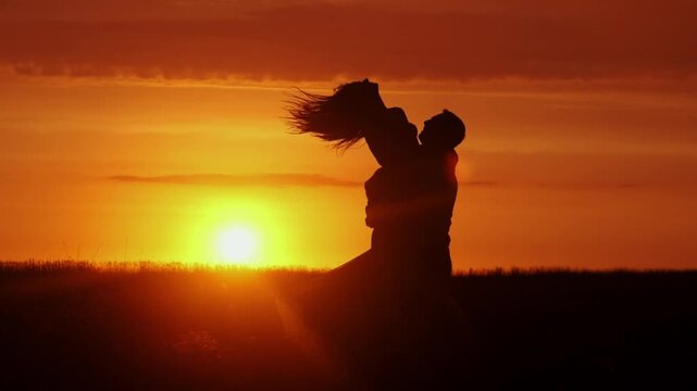 A couple hugging each other at sunset. The silhouettes are emphasized by the contrast of the bright sky and dark figures. Concept love story. Super slow-motion shot.