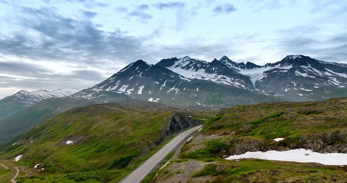 Footage over the highway crossing the mountainous landscape. Approaching the rocks covered with snow at backdrop. Alaska, USA.