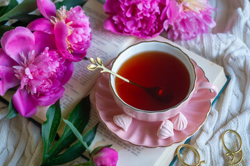 Delicate peony flowers and a cup of aromatic tea on the table.