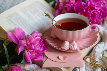 Delicate peony flowers and a cup of aromatic tea on the table.